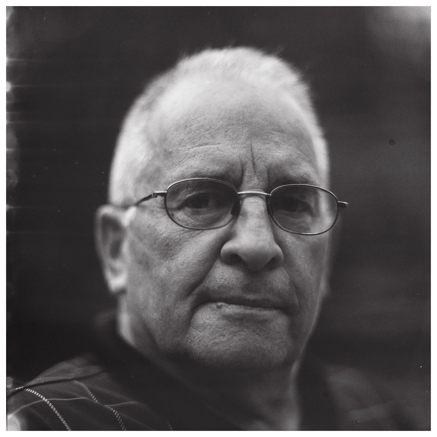 A man with glasses looks directly forward in a close-up portrait.