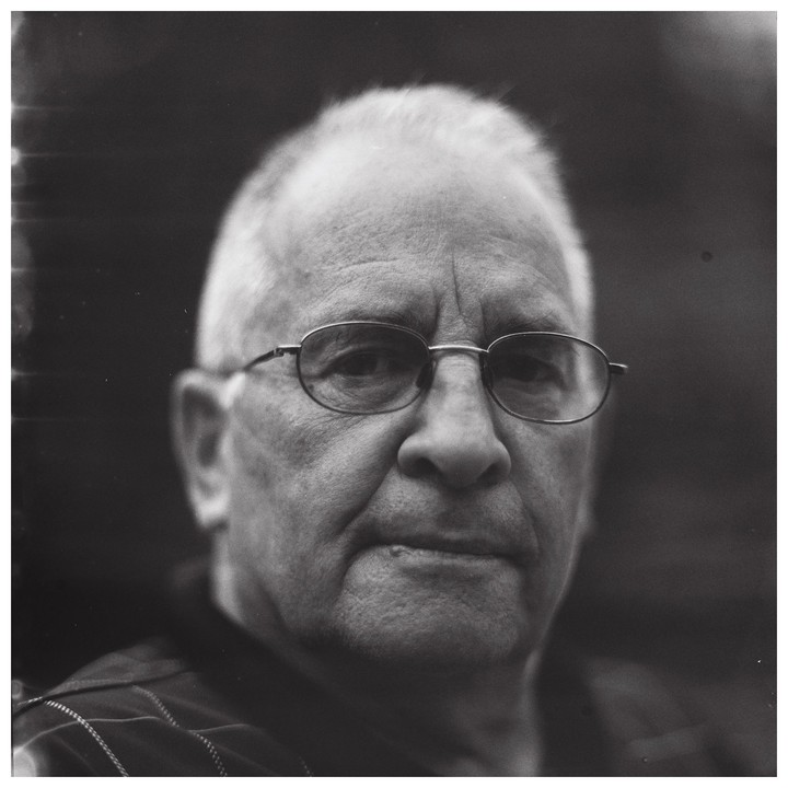 A man with glasses looks directly forward in a close-up portrait.