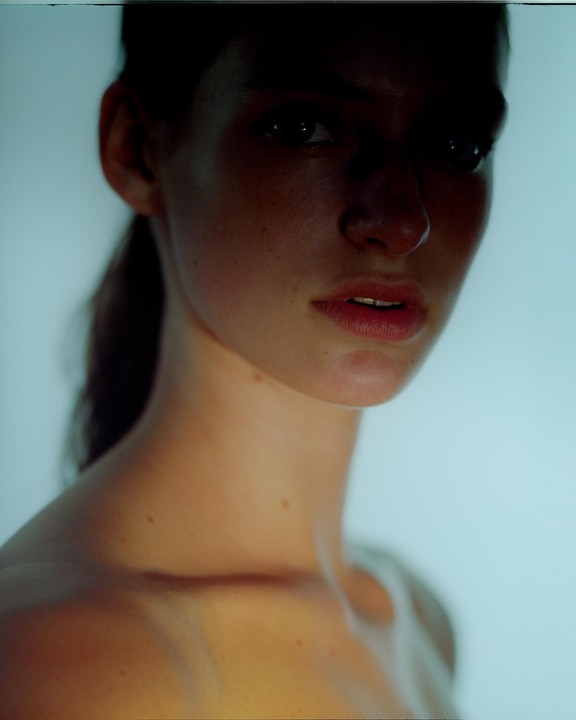 A woman's face and shoulder are illuminated by a soft light, with her face partially obscured by shadow.