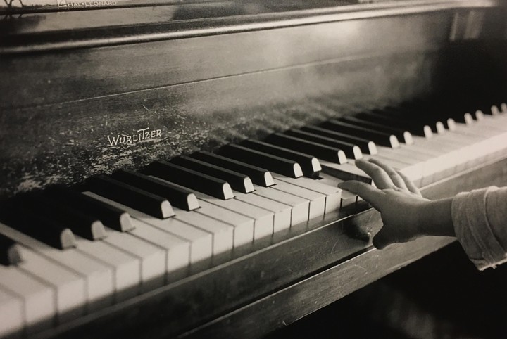 A child's hand presses a key on a Wurlitzer piano.