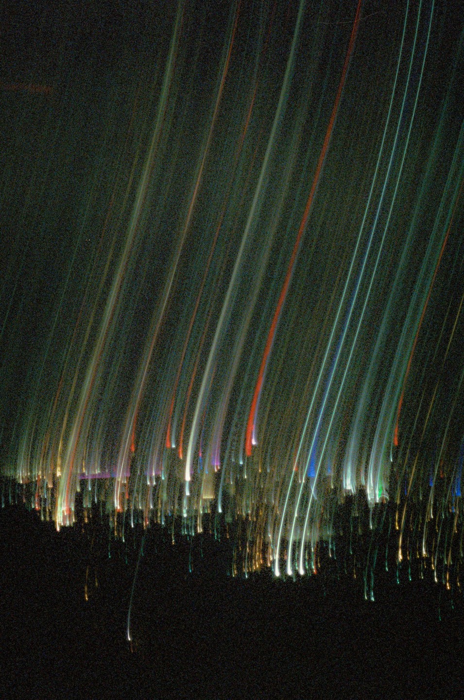 Streaks of colorful light descend from the top of the frame, with a blurred cityscape visible at the bottom.