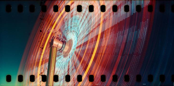 A long exposure shot captures the motion blur of a spinning carnival ride illuminated with red and blue lights against a dark sky.
