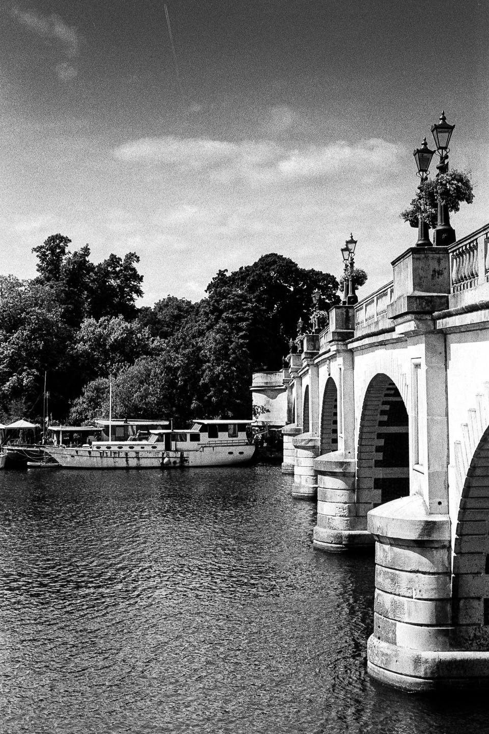 A boat is docked next to a bridge with multiple arches over a body of water, with trees in the background.