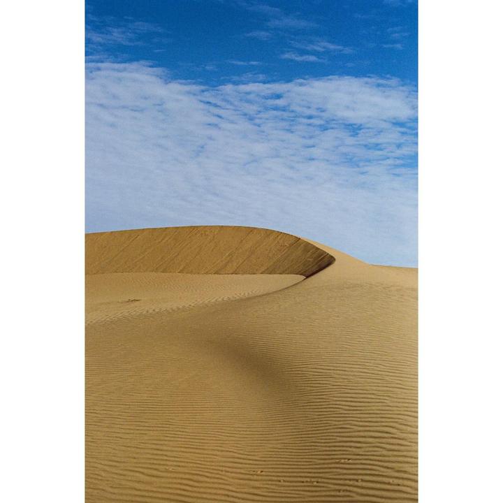 A large sand dune with ripples in the sand is visible under a blue sky with white clouds.