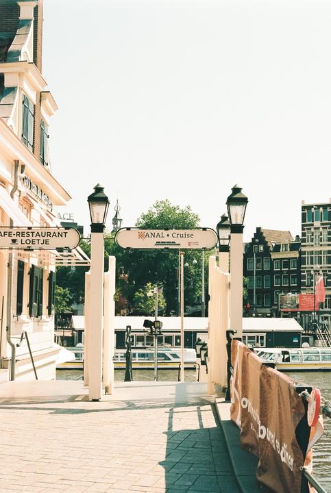A cafe and restaurant with a sign for a canal cruise is visible from a paved area next to a body of water.