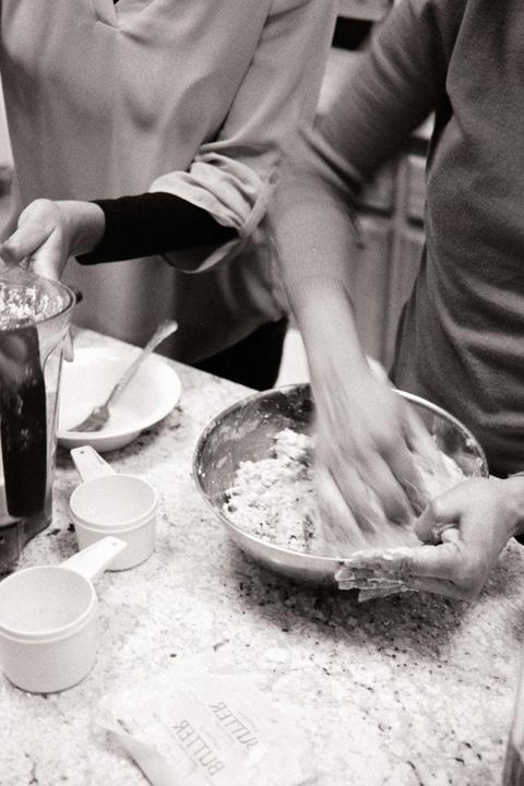 Two women are mixing dough in a bowl on a kitchen counter.