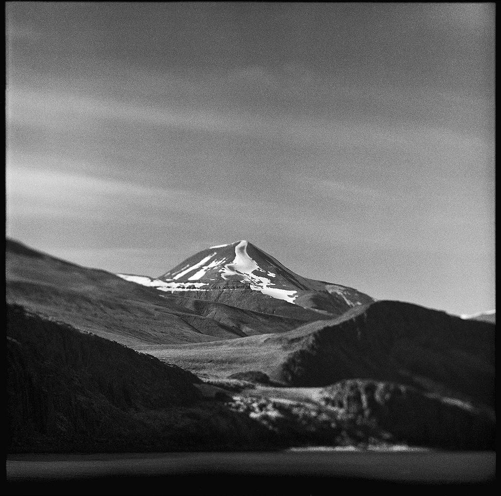 A snow-capped mountain rises above a valley with a body of water in the foreground.