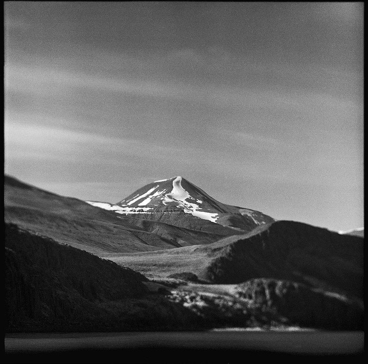 A snow-capped mountain rises above a valley with a body of water in the foreground.