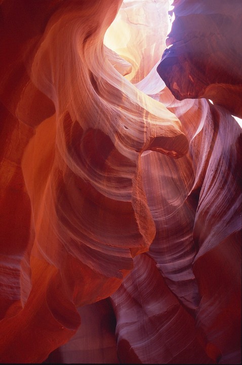 Light streams into a slot canyon with red and orange sandstone walls.