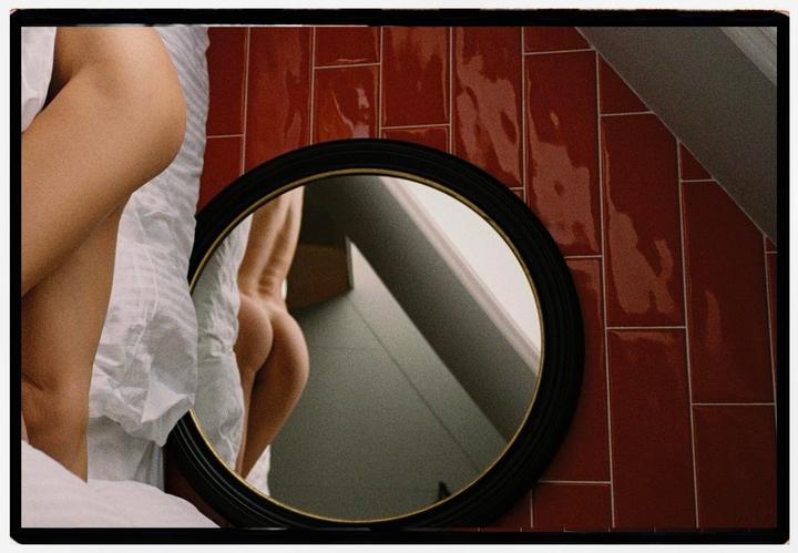 A woman's body is partially visible next to a round mirror reflecting her back and buttocks.