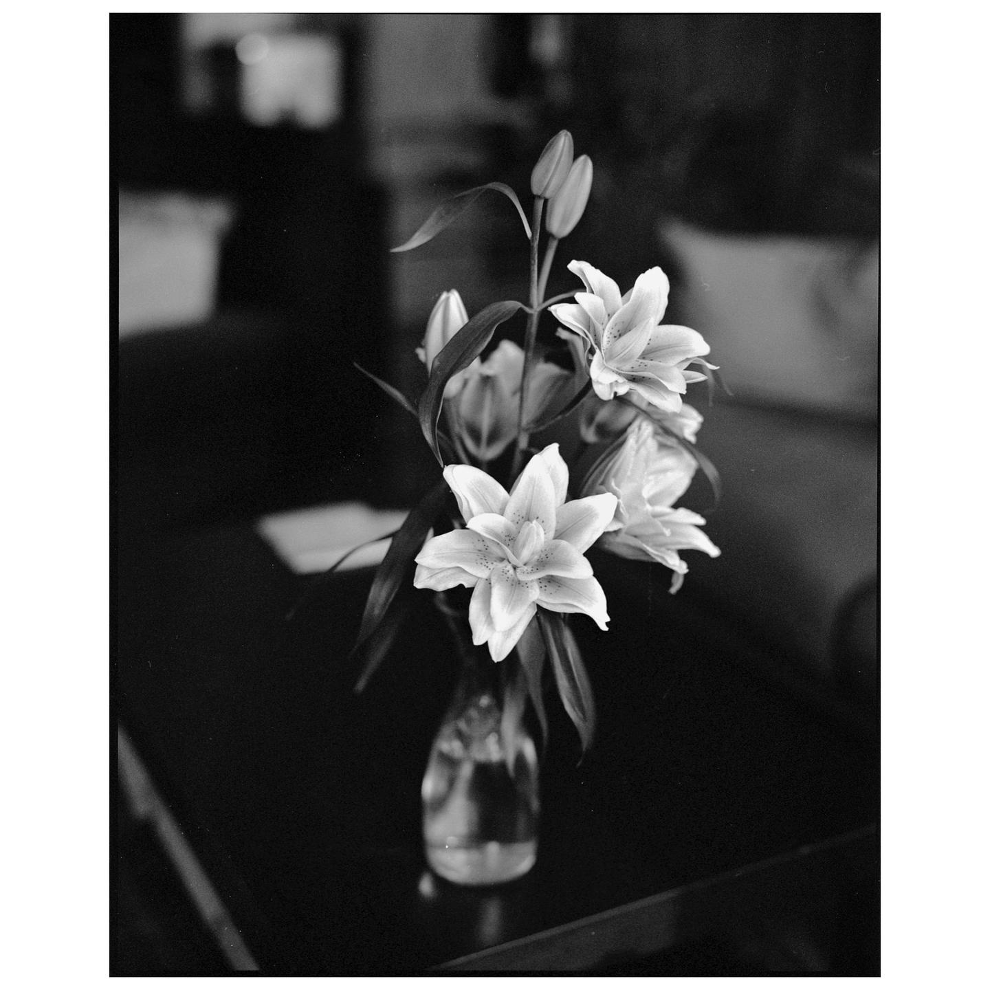 A bouquet of lilies in a glass vase sits on a dark surface.