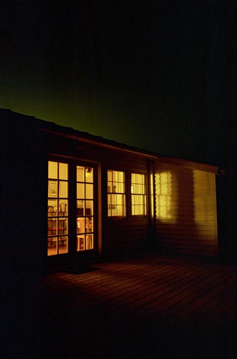 A house with illuminated windows and a wooden deck is visible at night.