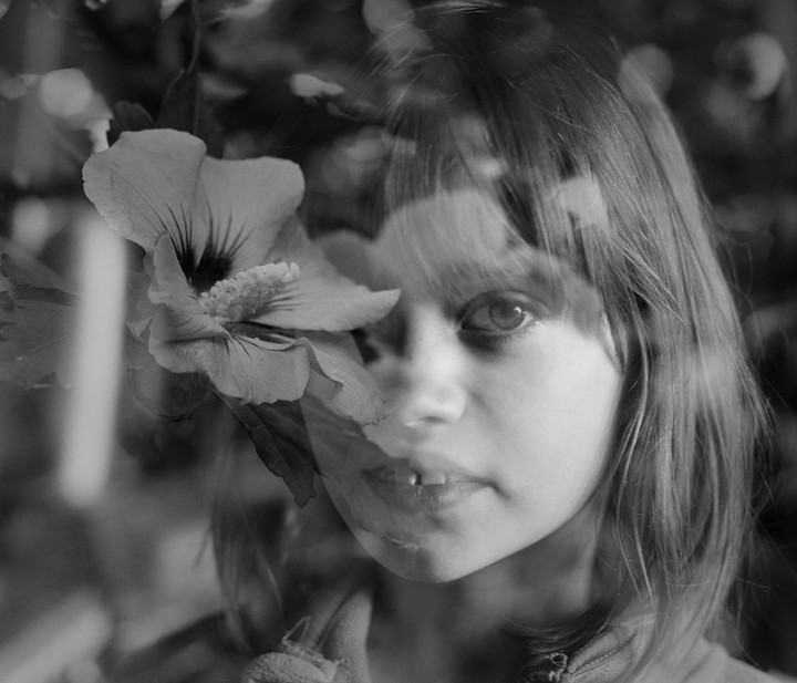 A girl's face is double exposed with a hibiscus flower.
