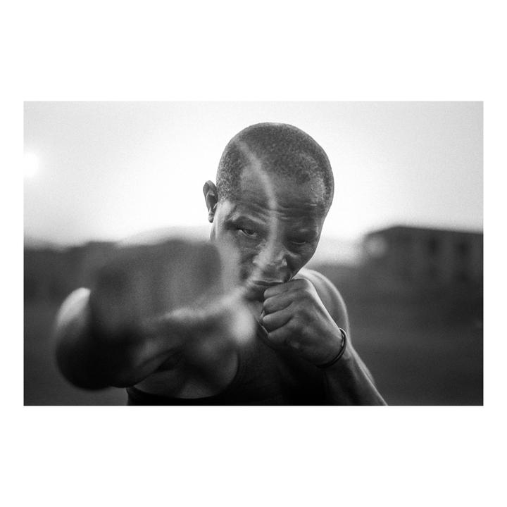 A man in a tank top is shown in a boxing stance, with one fist extended towards the viewer.