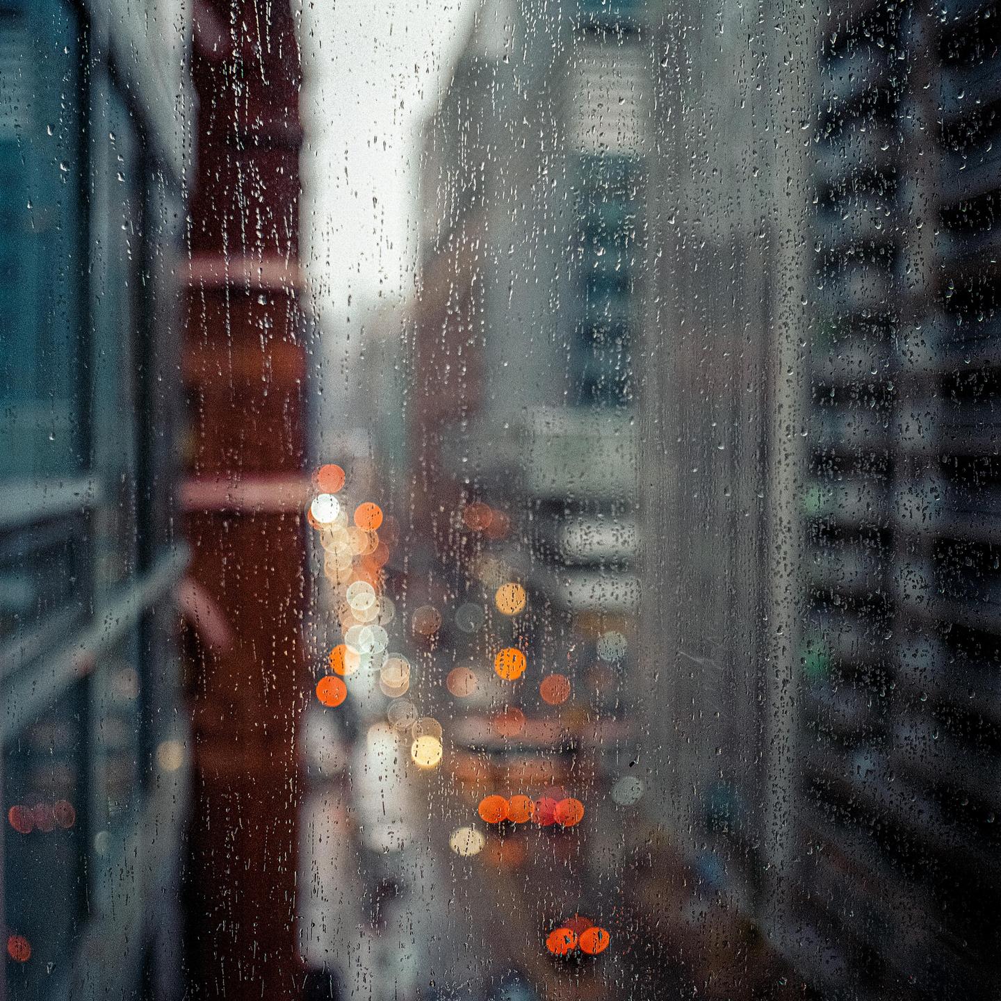 Raindrops cling to a window overlooking a blurry city street with bokeh lights.