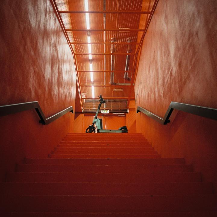 An electric scooter is parked at the top of a long, orange staircase with metal railings.
