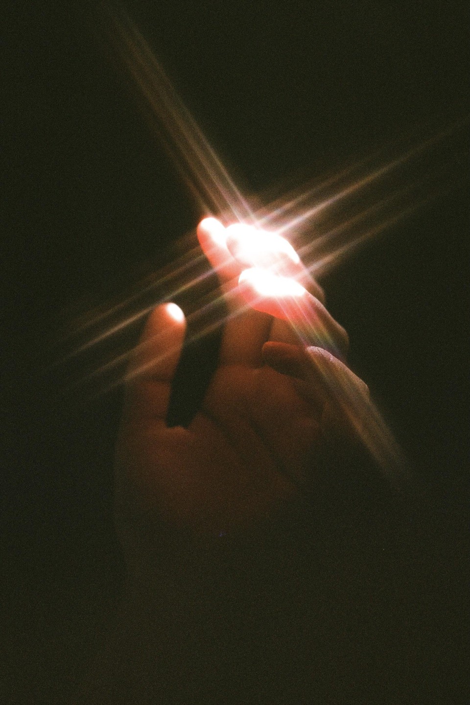 A hand is illuminated by a bright light source, creating a starburst effect.