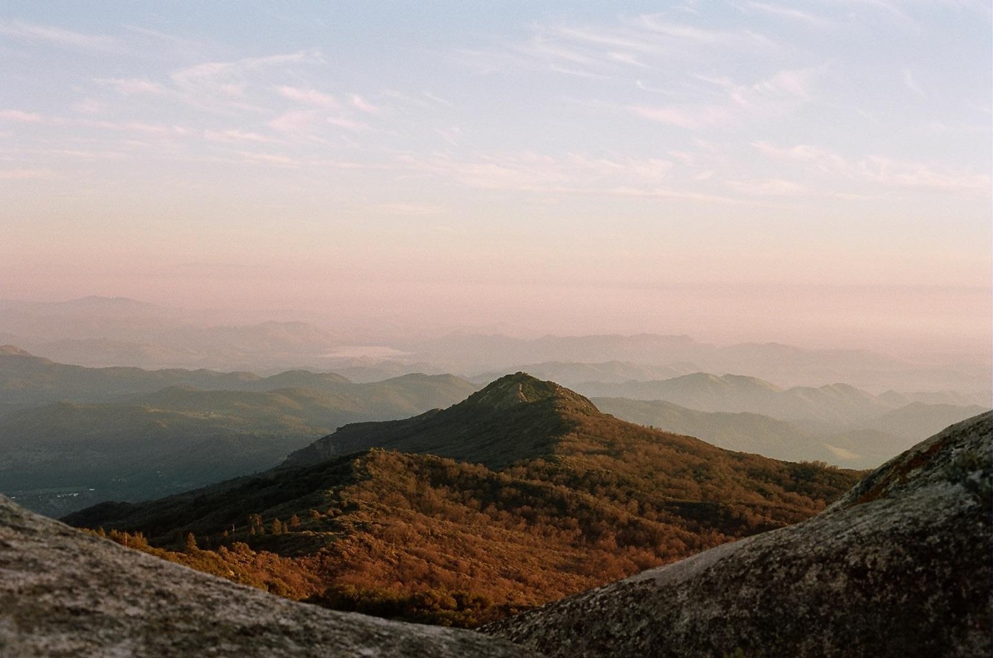 A mountain range is visible under a hazy sky with a prominent peak in the middle ground and large rocks in the foreground.