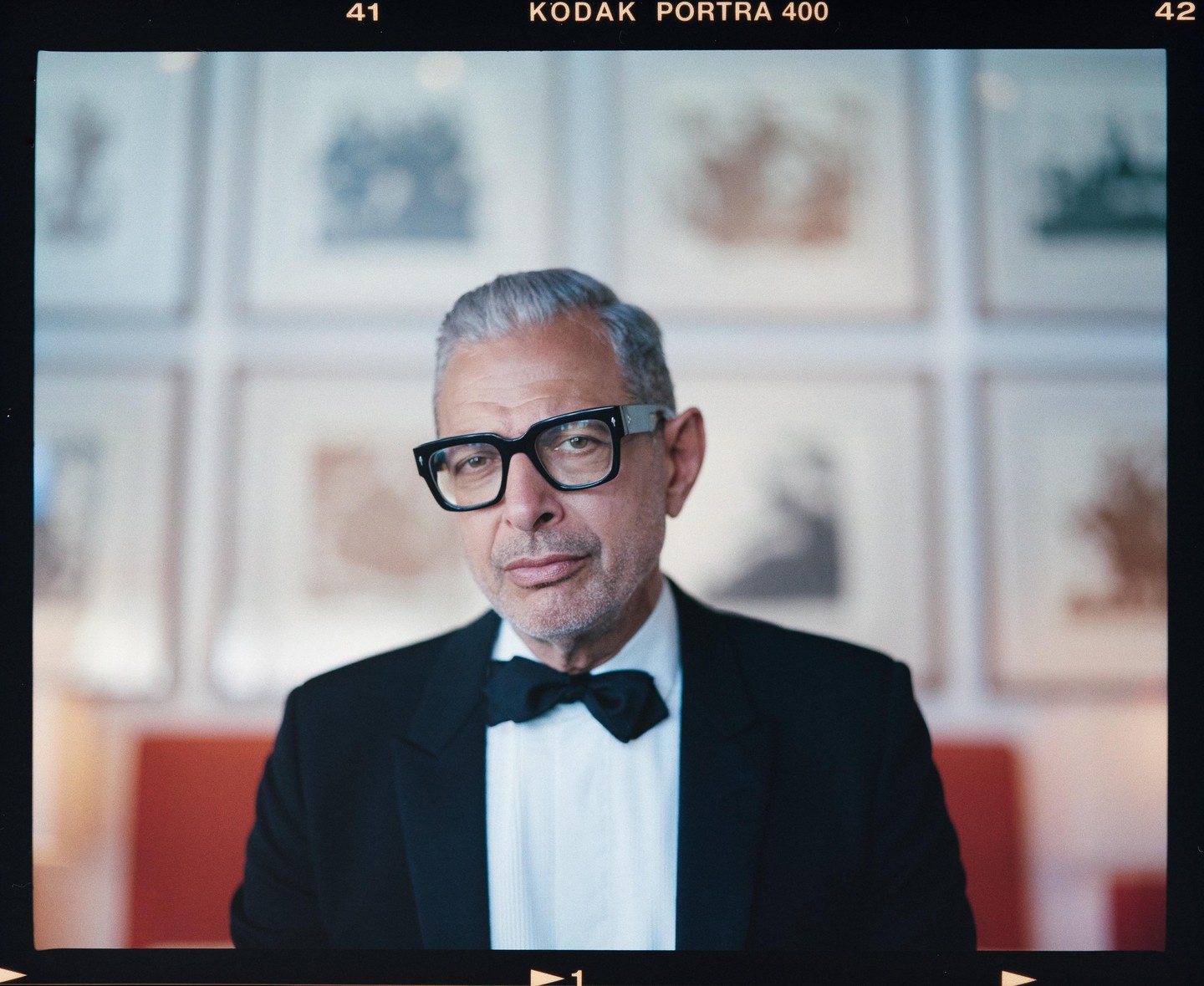 A man in a tuxedo and glasses looks directly at the viewer.