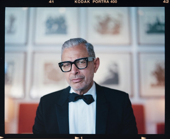 A man in a tuxedo and glasses looks directly at the viewer.