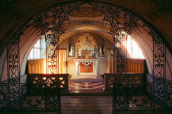 Sunlight streams through the windows of a chapel, illuminating an altar with religious paintings and ornate ironwork.
