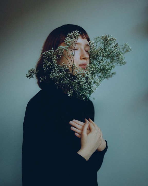 A woman with closed eyes holds a bouquet of baby's breath flowers in front of her face.