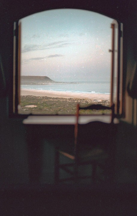 A view of a beach and mountain is seen through an open window.