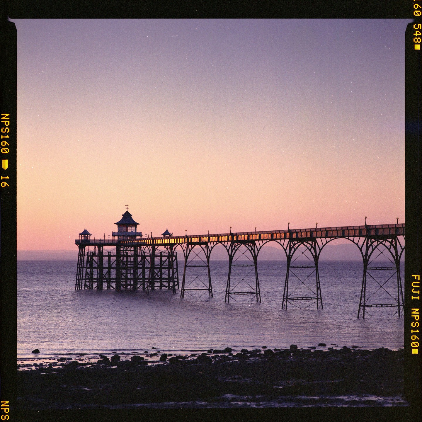 A pier extends over the water under a colorful sky at dusk.
