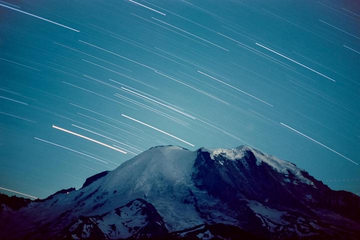 A snow-capped mountain stands under a night sky filled with star trails.