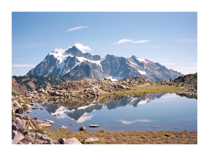 A snow-capped mountain range is reflected in a still lake under a clear sky.