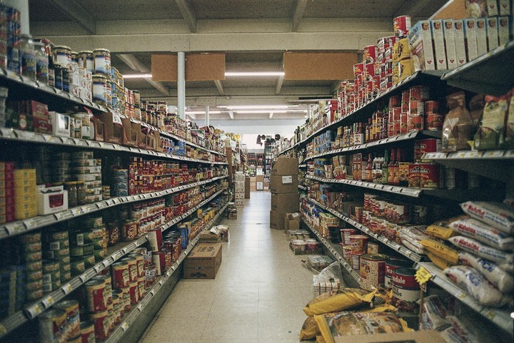 A narrow aisle in a grocery store is lined with shelves packed with various food products and boxes.