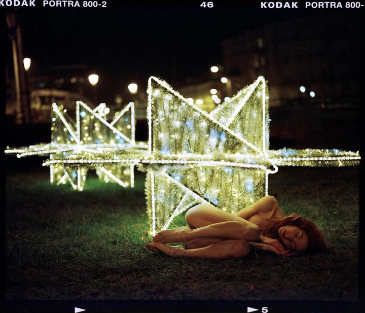 A woman sleeps on the grass next to a large illuminated star decoration at night.