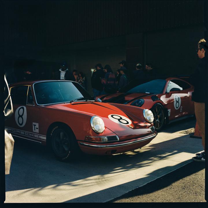 Two red Porsche cars with the number eight on them are parked in a garage with people standing around them.