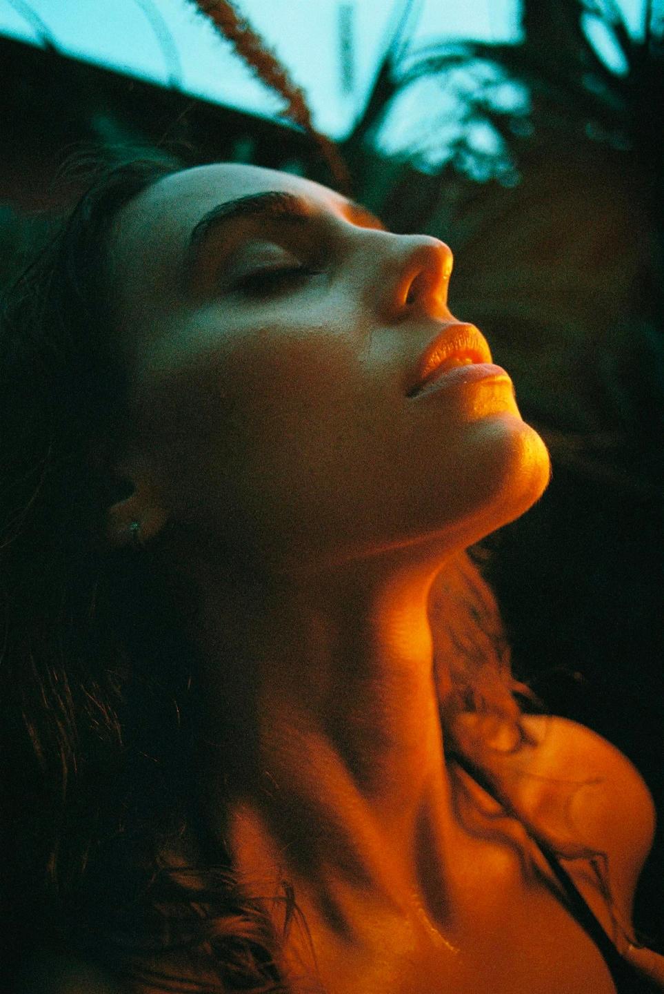 A woman with closed eyes and her head tilted back is illuminated by warm light from below.