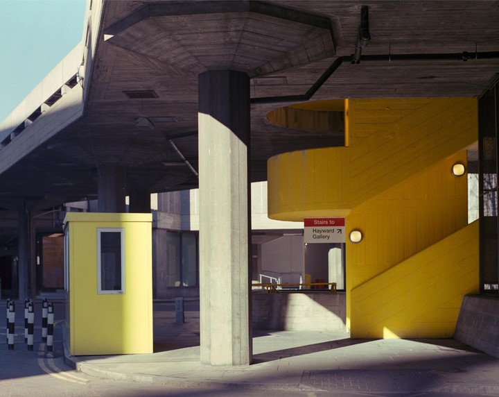 A bright yellow booth and a yellow staircase with a sign for the Hayward Gallery are visible under a concrete overpass.