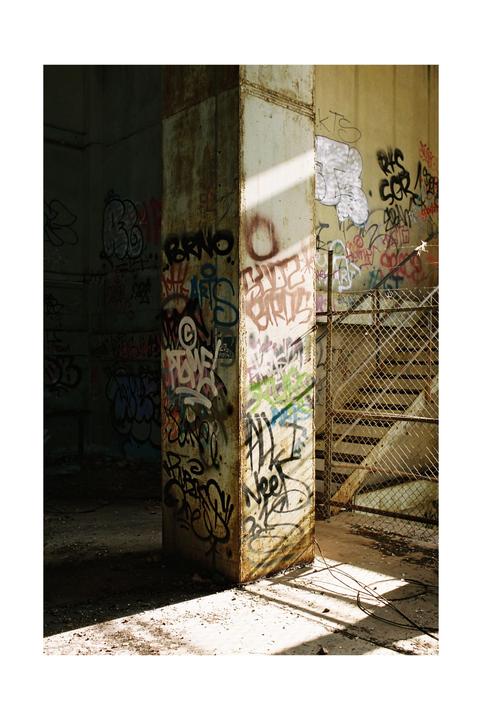 Sunlight illuminates a graffiti-covered pillar and wall in an abandoned building.