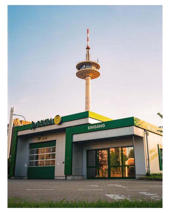 A tall communication tower stands behind a modern building with green accents and large windows.