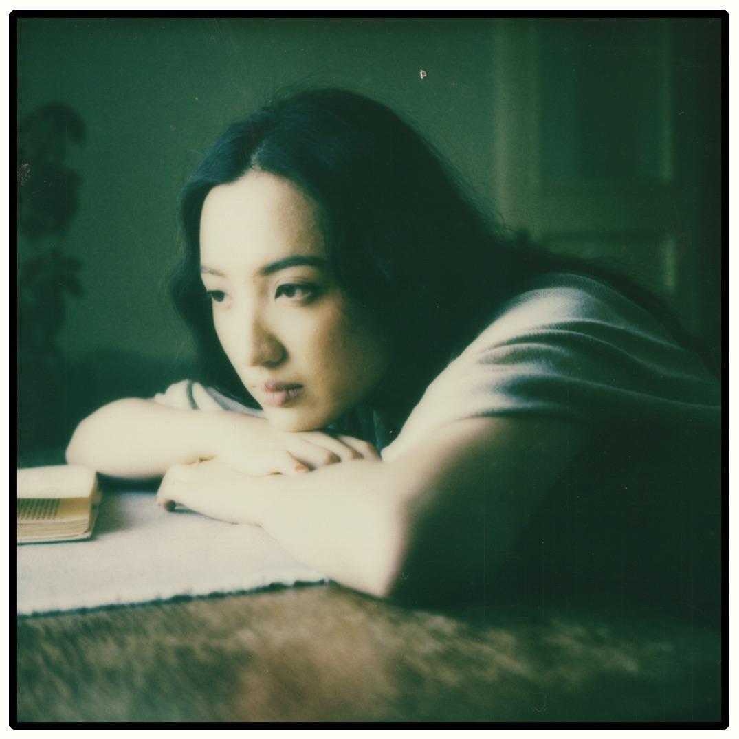 A woman rests her head on her arms on a table next to a book.