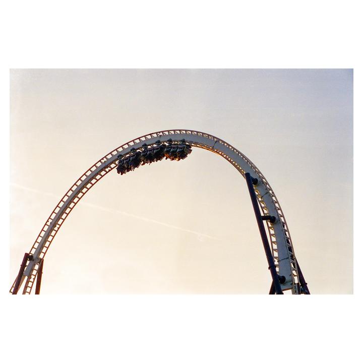 A rollercoaster car with people is upside down on a loop against a light sky.