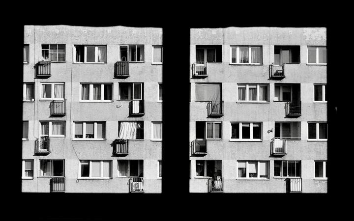Two sections of a multi-story building facade with many windows and balconies are separated by a black vertical strip.