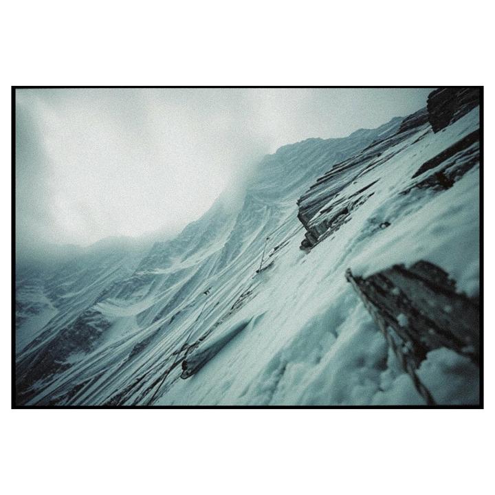 A snow-covered mountain slope with rocky outcrops is visible under a cloudy sky.
