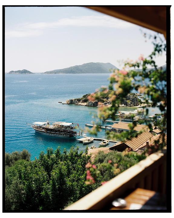 A boat is docked in a bay with buildings and trees on the shore, and islands in the distance.