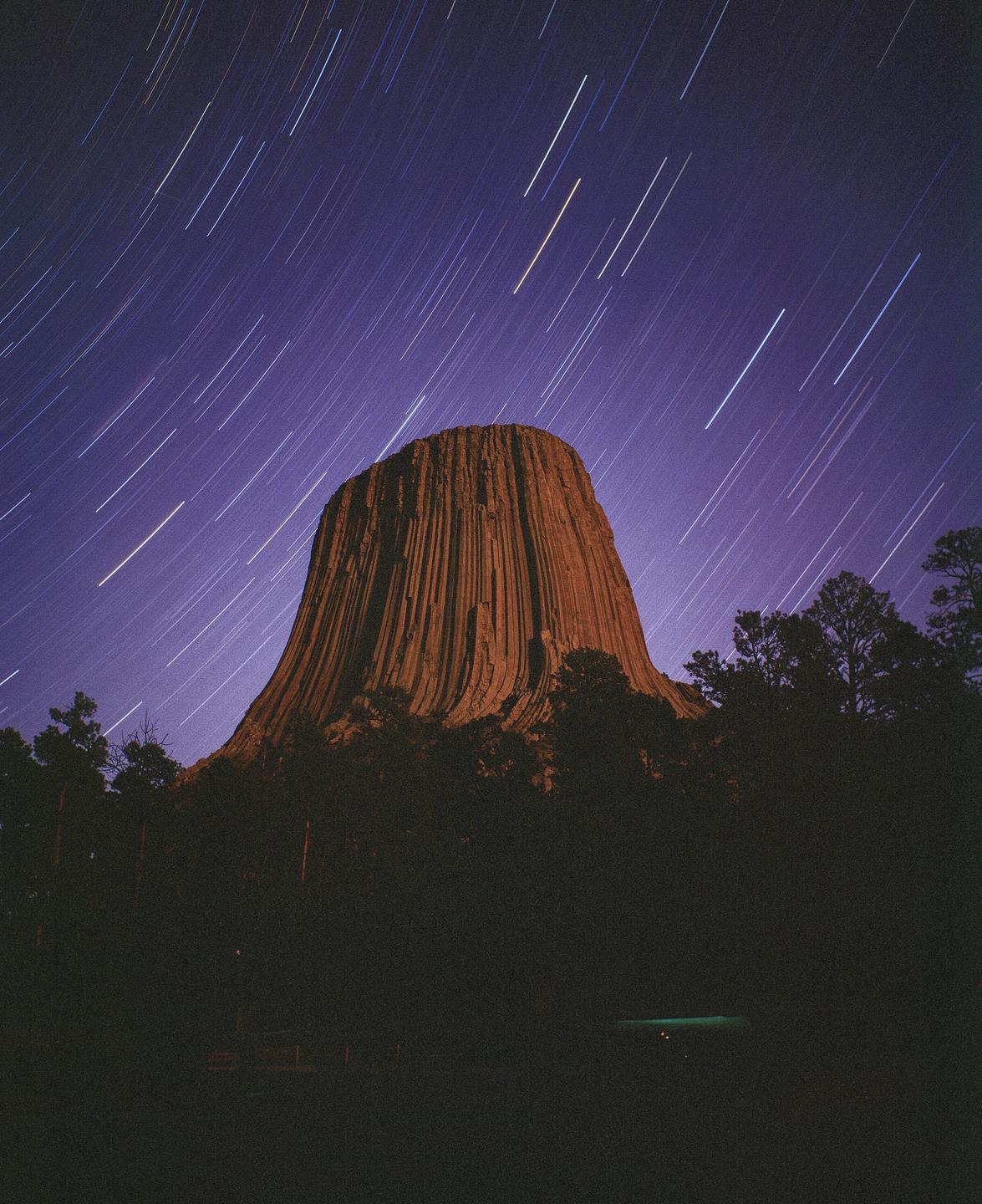A large rock formation stands tall against a night sky filled with star trails.