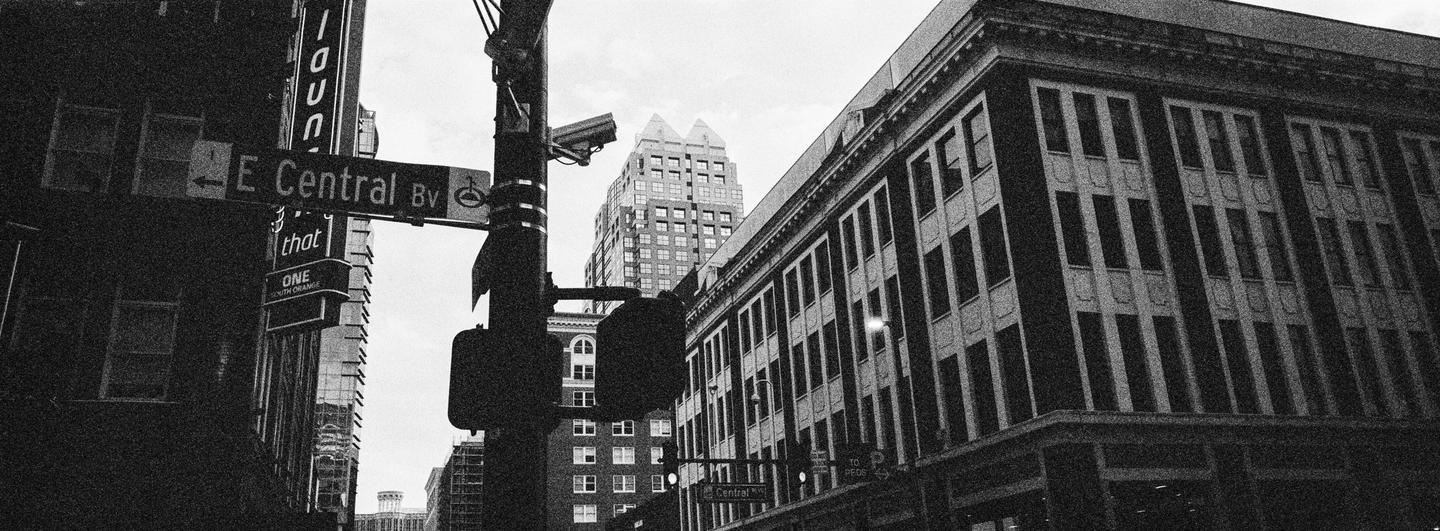 A street sign for E Central Boulevard is visible among tall buildings in a city.
