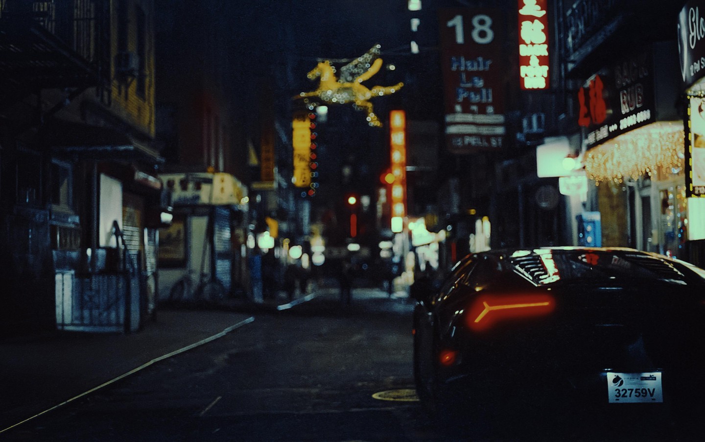 A black sports car with illuminated taillights is parked on a city street at night, surrounded by neon signs and blurred lights.