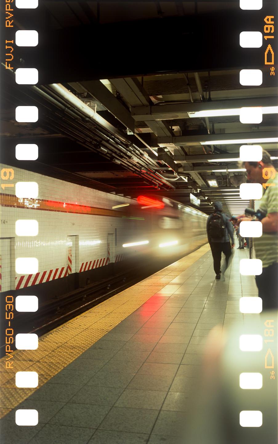 A subway train with blurred lights speeds through a station platform where people are waiting.