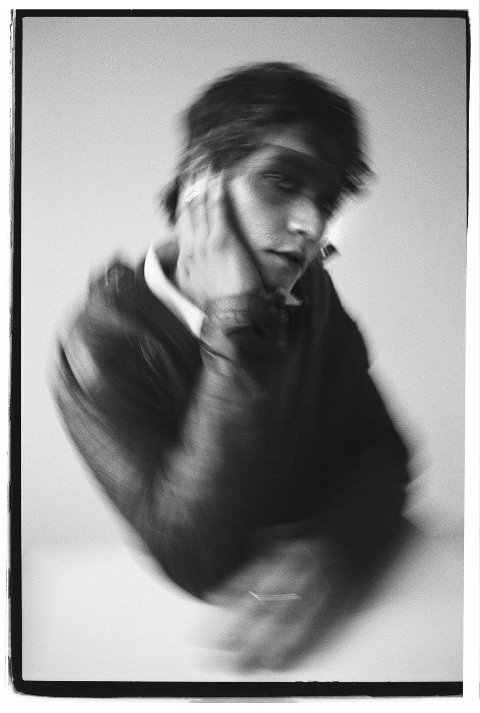 A man with his hand on his face is captured in a blurry, black and white portrait.