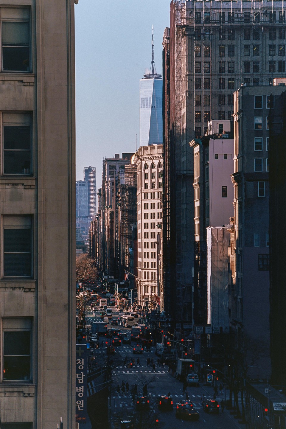 A tall skyscraper rises above a busy street lined with buildings and traffic.