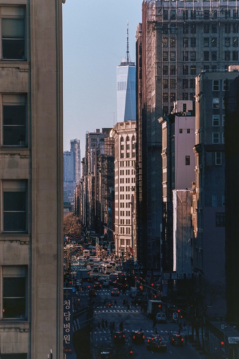 A tall skyscraper rises above a busy street lined with buildings and traffic.