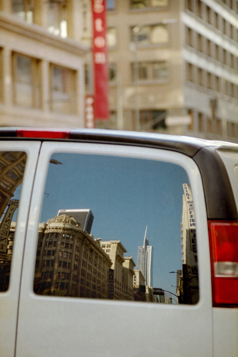 A city street is reflected in the window of a white van.